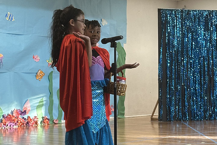 Two girls act out a scene on stage