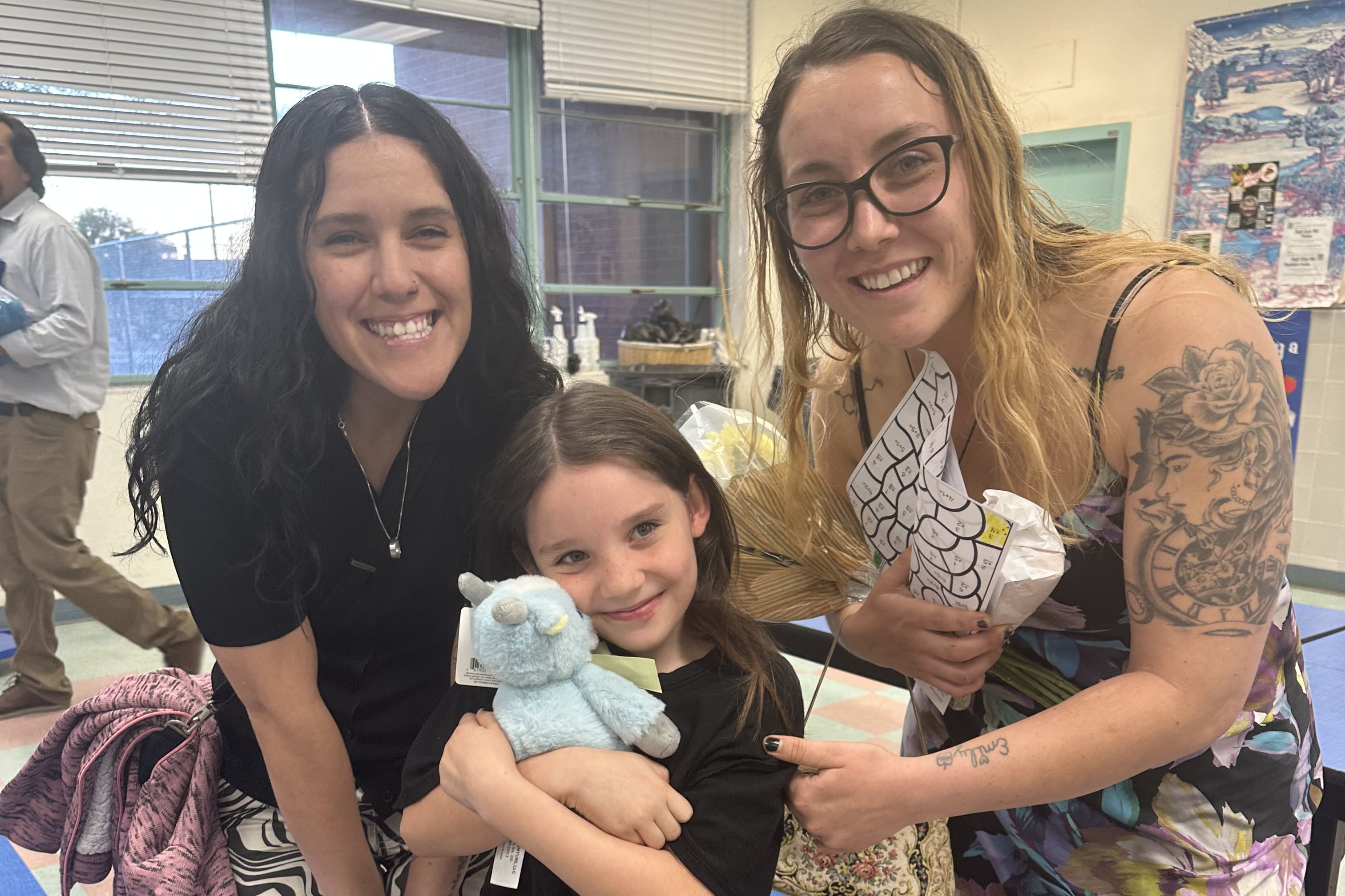 Two women smile with a girl holding a stuffed animal