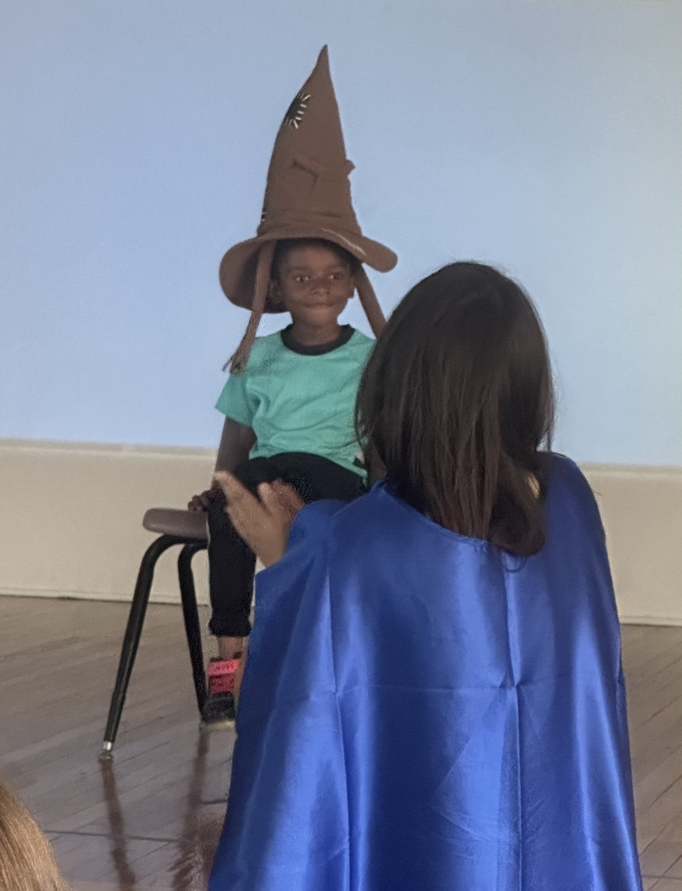 A little boy in a green shirt wears the sorting hat