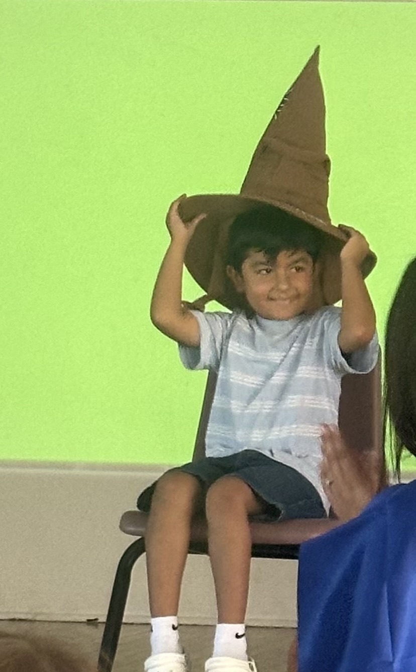 A little boy in a striped shirt holds onto the sorting hat