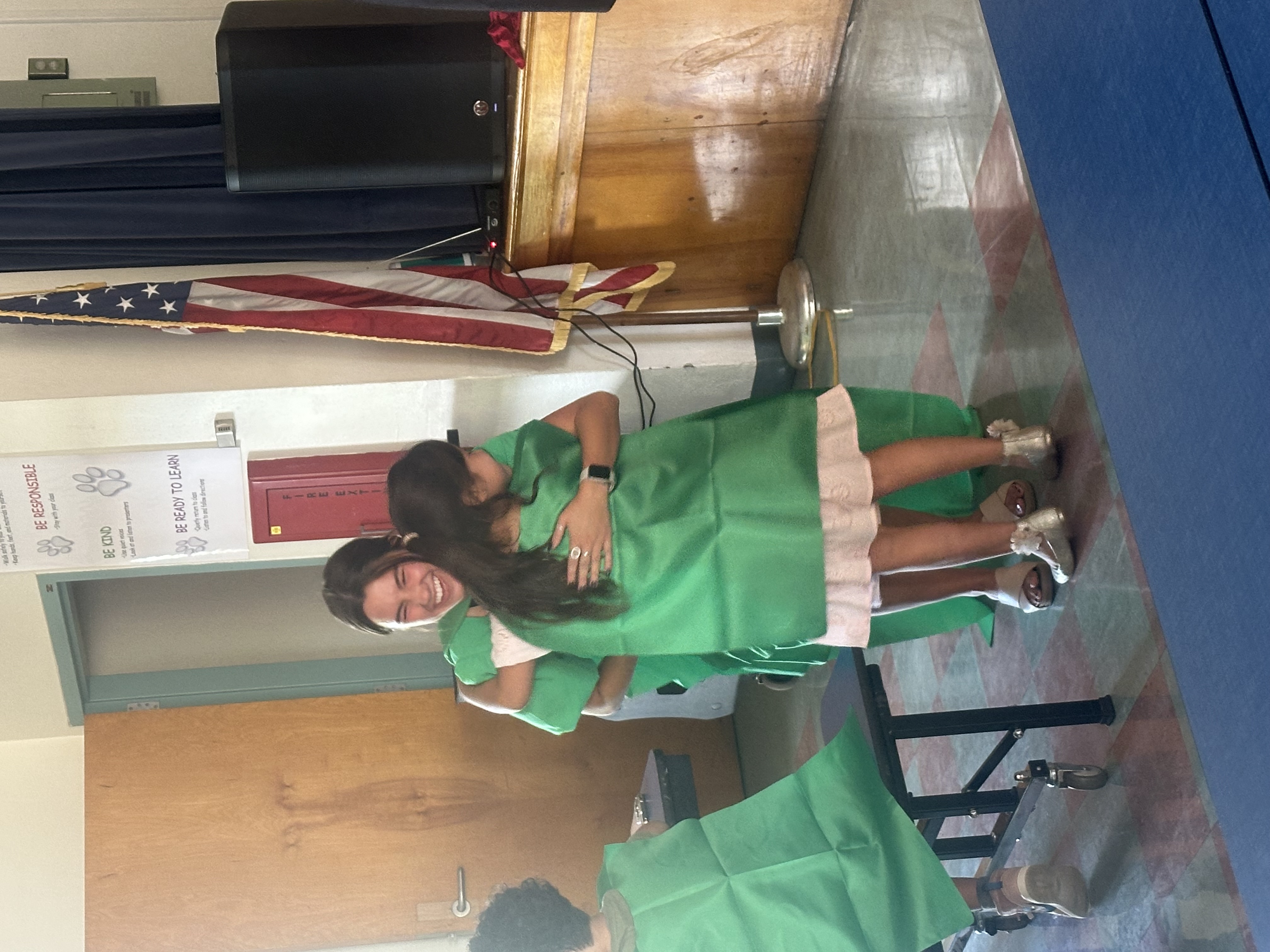 A little girl in a green cape hugs her teacher