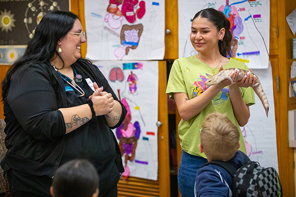 A woman smiles as another woman holds up a giant lizard
