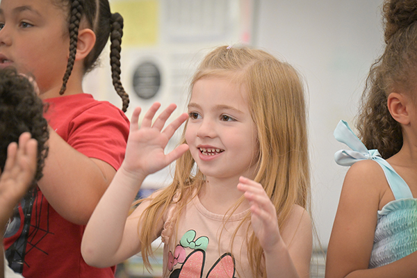 A girl excitedly claps her hands during a performance with her classmates