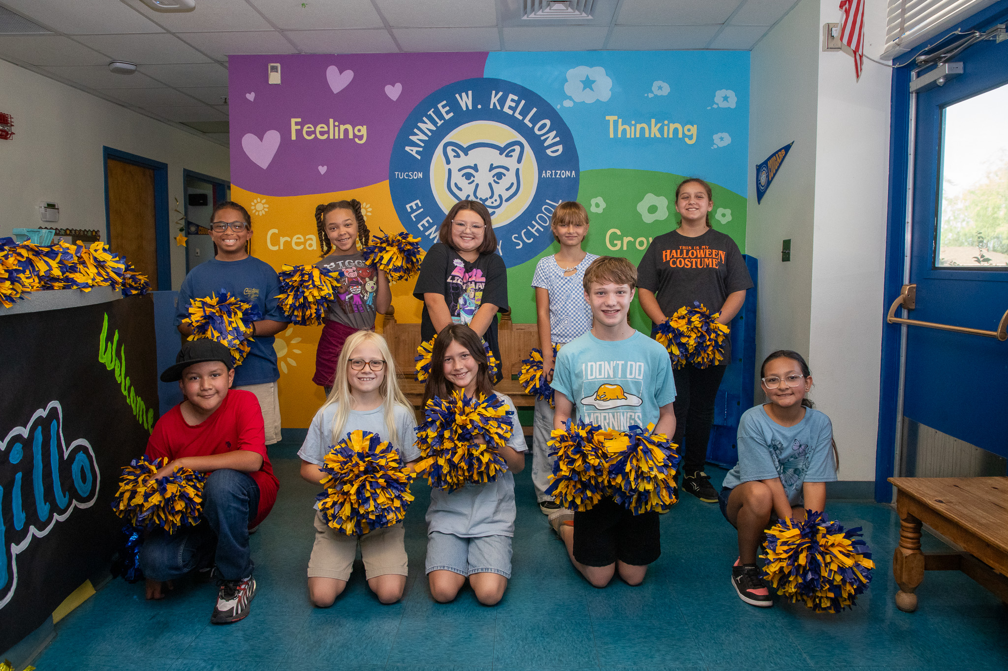 A group of students pose with pom-poms in front of a Kellond backdrop